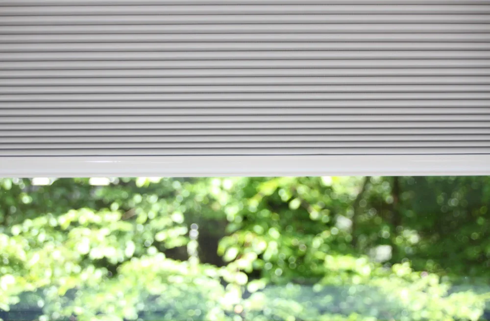 Närbild på ett solskydd som är halvt neddraget framför gröna träd